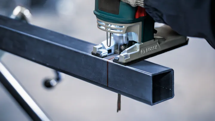 Una persona que usa equipo de seguridad utiliza una sierra caladora para cortar una viga de metal.