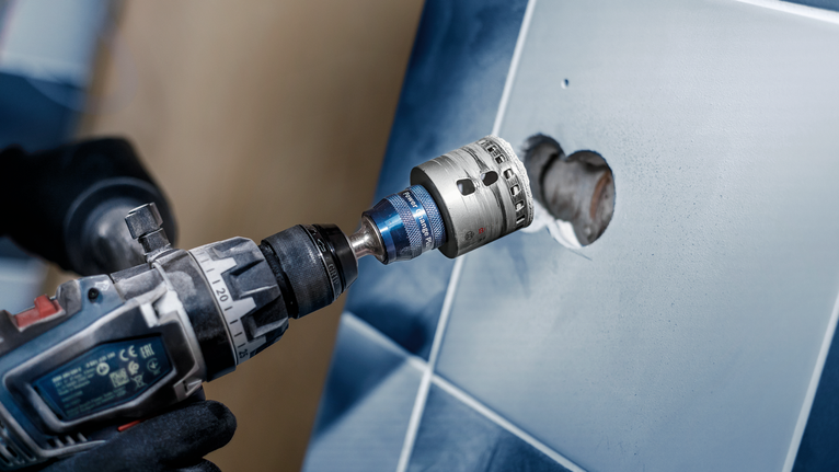 Una persona que usa equipo de seguridad utiliza un taladro eléctrico para cortar un agujero en una pared de azulejos.