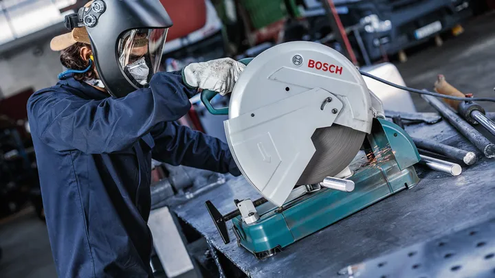 Una persona que usa equipo de seguridad corta tubos de metal con una sierra circular estacionaria.