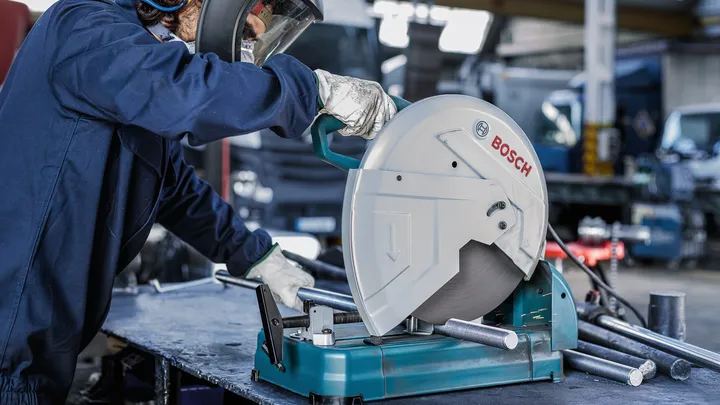 Una persona que usa equipo de seguridad opera una sierra circular para cortar tubos de metal.