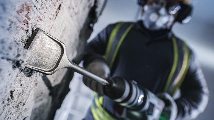 Una persona que usa equipo de seguridad utiliza un martillo rotatorio para cincelar una pared de hormigón.