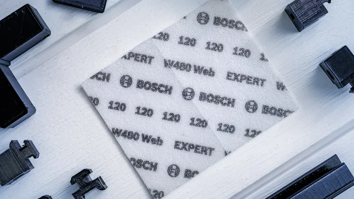 Se coloca una hoja de lija abrasiva blanca con especificaciones impresas sobre una superficie de madera clara.