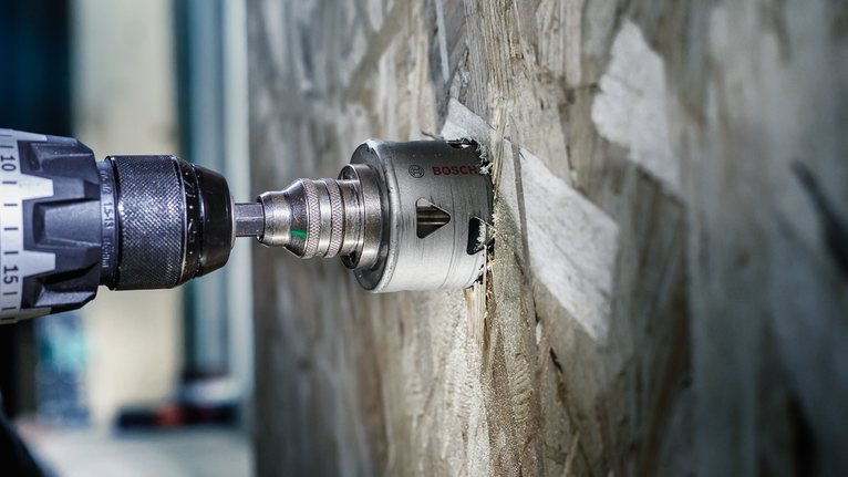 Taladro eléctrico con accesorio de sierra de corona cortando una pared de madera.