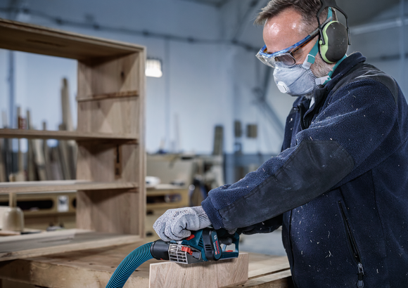 Una persona que usa equipo de seguridad lija una tabla de madera en un taller.