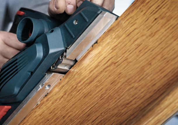 Una persona utiliza una cepilladora eléctrica para alisar el borde de una tabla de madera.