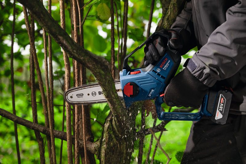 Una persona que usa equipo de seguridad utiliza una sierra podadora inalámbrica para cortar la rama de un árbol.
