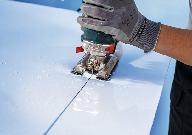 Un trabajador que usa equipo de seguridad utiliza una sierra caladora para cortar una línea recta en un panel blanco.