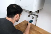 Persona verificando el nivel de humedad en una encimera de madera cerca de la plomería debajo de una caldera.