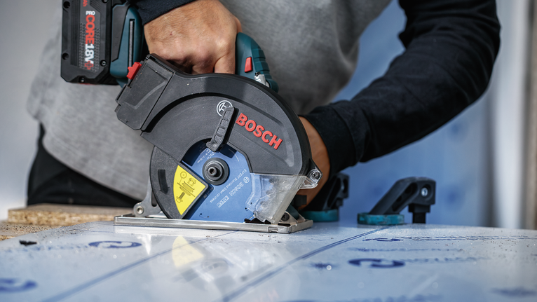 Una persona que usa equipo de seguridad utiliza una sierra circular para cortar un tablero laminado.