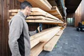 Una persona mide la madera apilada con un medidor de humedad en un área de almacenamiento de madera.