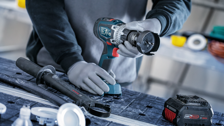 Una persona que usa equipo de seguridad perfora una superficie de trabajo con una herramienta eléctrica inalámbrica.