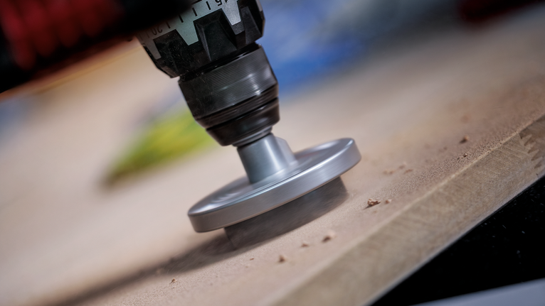 Herramienta rotatoria lijando el borde de una tabla de madera.