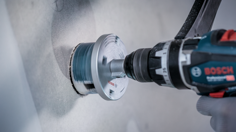 Persona que usa equipo de seguridad perforando un agujero circular en una pared.