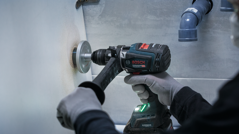 Una persona que usa equipo de seguridad perfora un agujero en una pared con una herramienta eléctrica.