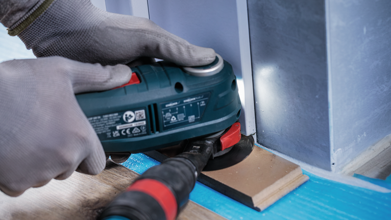 Una persona que usa equipo de seguridad utiliza una herramienta eléctrica para lijar madera cerca de una pared.