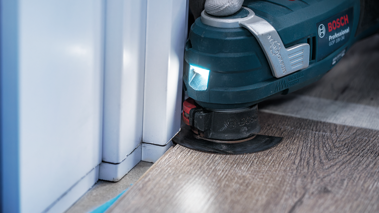 Herramienta multiusos oscilante recortando pisos laminados cerca del marco de una puerta.