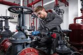 Una persona que usa equipo de seguridad utiliza una llave de impacto inalámbrica para apretar una válvula en un entorno industrial.