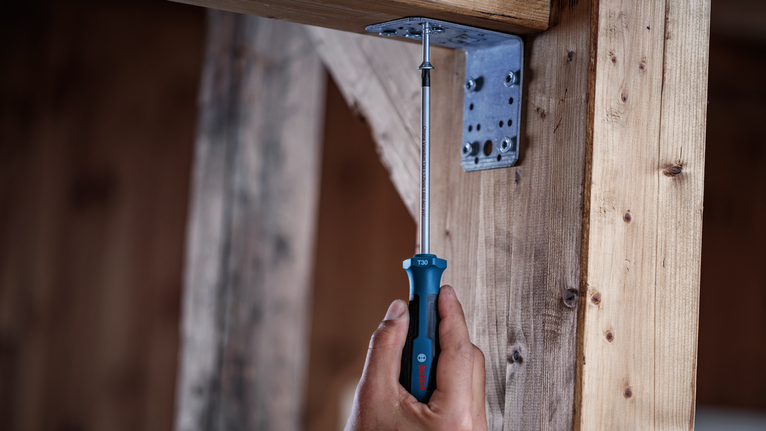Una persona aprieta un tornillo en un soporte metálico sobre un marco de madera.