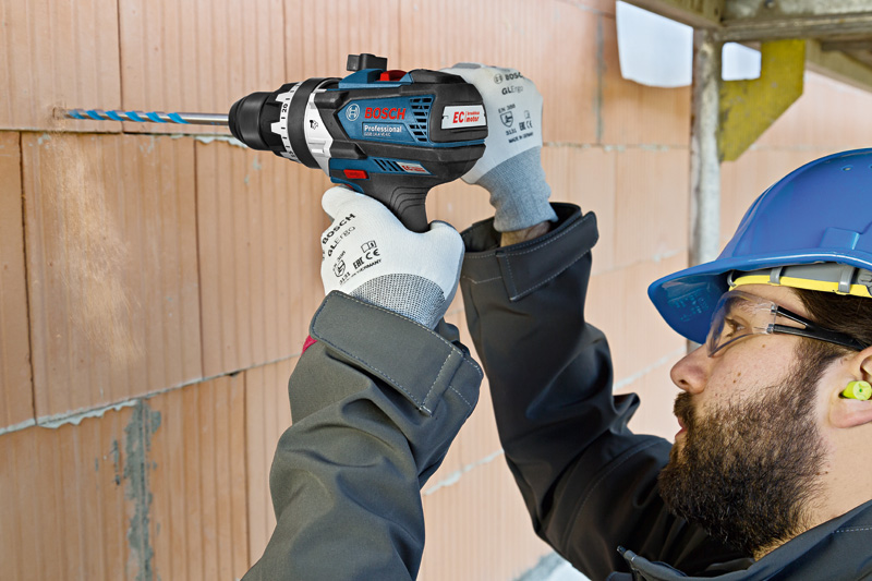 Un hombre usa un taladro Bosch Professional en una pared de ladrillos.