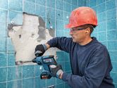 Una persona que usa equipo de seguridad utiliza un martillo rotatorio inalámbrico para quitar azulejos de la pared.