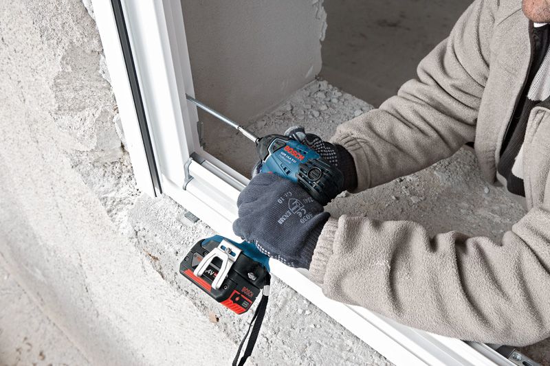 Una persona que usa equipo de seguridad utiliza un destornillador de impacto inalámbrico para fijar el marco de una ventana.