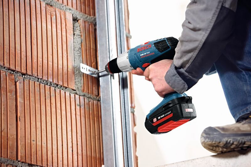 Una persona fija un soporte de metal a una pared de ladrillos utilizando un taladro combinado inalámbrico.