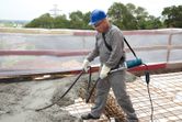 Una persona que usa equipo de seguridad opera un vibrador de concreto en un sitio de construcción.