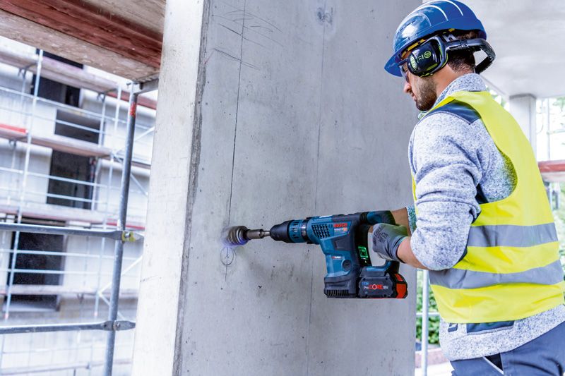 Una persona que usa equipo de seguridad utiliza un martillo perforador inalámbrico para perforar hormigón.