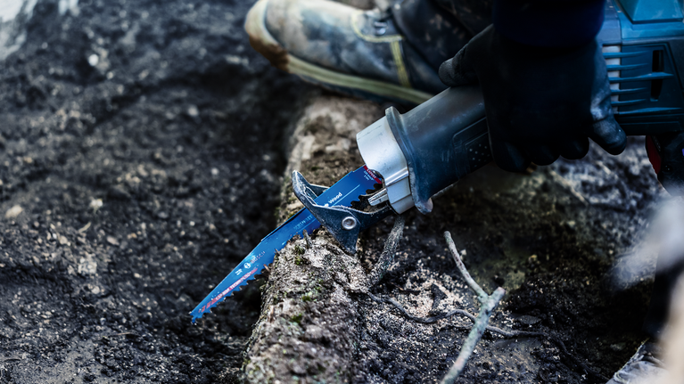 Una persona que usa equipo de seguridad utiliza una sierra alternativa para cortar la raíz de un árbol.