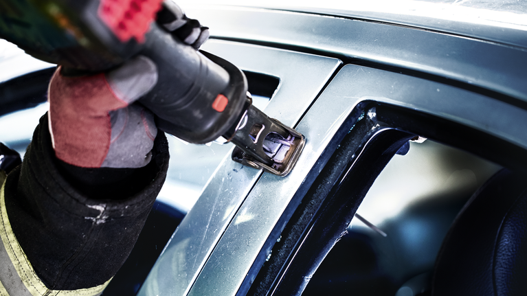 Una persona que usa equipo de seguridad utiliza una herramienta eléctrica para cortar el marco de la ventana de un automóvil.