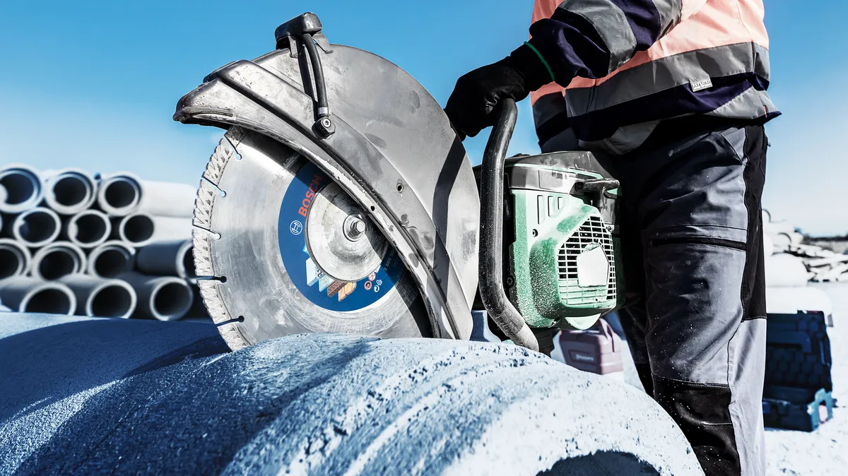 Una persona que usa equipo de seguridad corta un tubo de hormigón de gran tamaño con una sierra eléctrica.