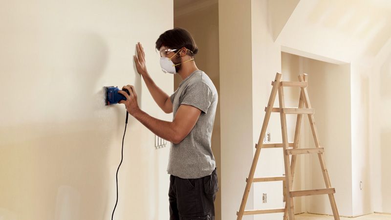 Hombre lijando pared en interior.