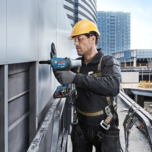 Una persona que usa equipo de seguridad utiliza un taladro eléctrico para fijar paneles en el exterior de un edificio.
