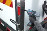 Una persona que usa equipo de seguridad utiliza una llave de impacto para asegurar un perno en una puerta de metal.