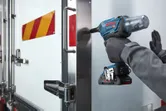Una persona que usa equipo de seguridad utiliza un destornillador de impacto inalámbrico en la puerta metálica de un camión.