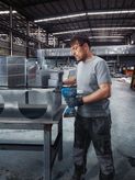 Una persona que usa equipo de seguridad asegura conductos de metal utilizando una pistola remachadora inalámbrica.