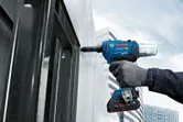 Una persona que usa equipo de seguridad fija un panel de metal con una pistola remachadora inalámbrica.
