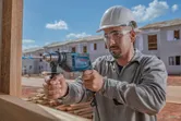 Una persona que usa equipo de seguridad perfora madera en un sitio de construcción.