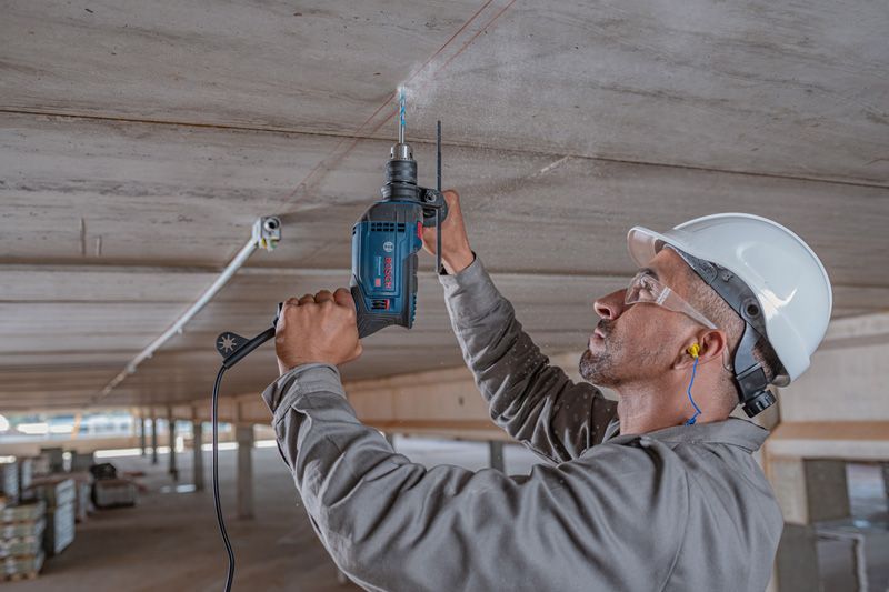 Una persona que usa equipo de seguridad perfora un techo de concreto usando un taladro de impacto.