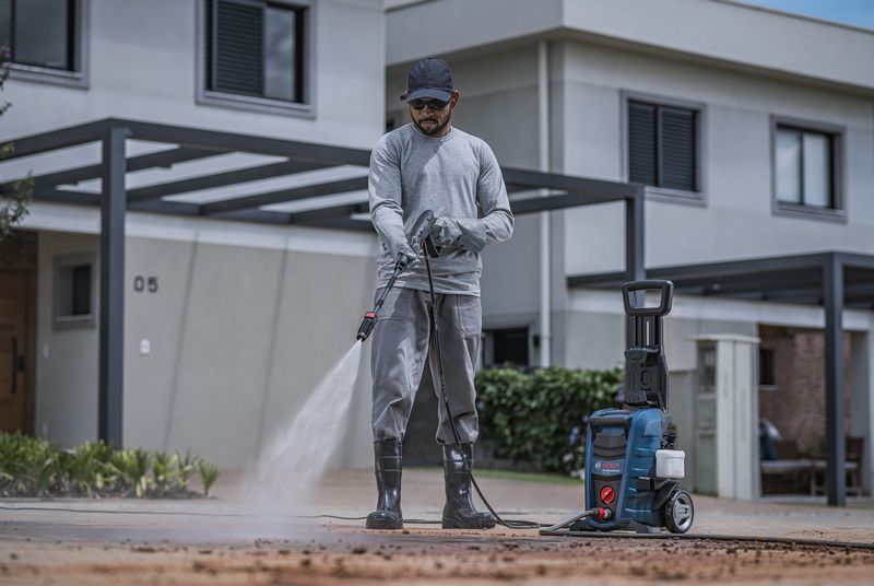 Una persona que usa equipo de seguridad limpia un camino de entrada con una hidrolavadora.