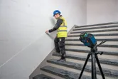 Una persona que lleva equipo de seguridad alinea una marca en la pared utilizando un nivel láser en unas escaleras.