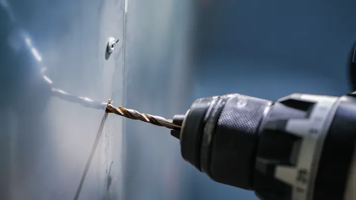 Un taladro eléctrico hace un agujero en un panel de metal.