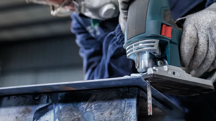 Una persona que usa equipo de seguridad utiliza una sierra caladora para cortar una lámina de metal.