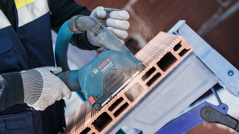 Una persona que usa equipo de seguridad corta un ladrillo hueco con una herramienta eléctrica.