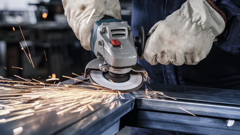 Una persona que usa equipo de seguridad muele metal, produciendo chispas brillantes.