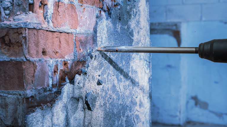 Taladro cincel rompiendo hormigón de una pared de ladrillos.