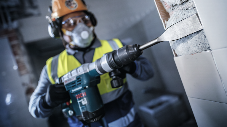 Una persona que usa equipo de seguridad utiliza una herramienta de demolición para quitar azulejos de la pared.