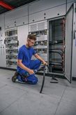 Una persona que usa equipo de seguridad corta un cable grueso frente a un panel eléctrico abierto.