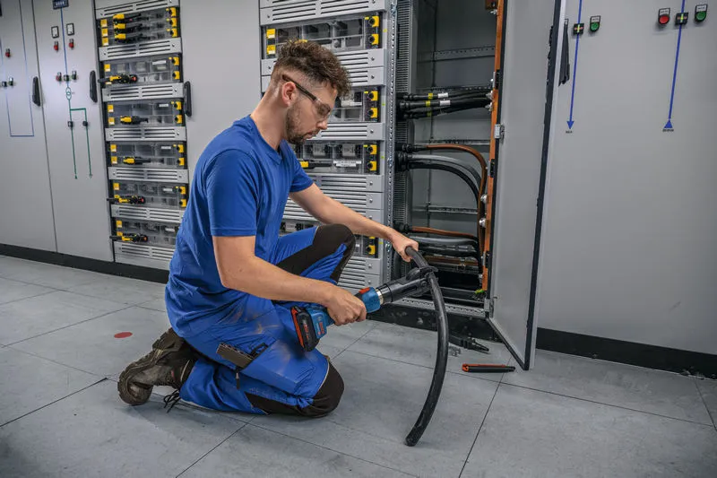 Una persona que usa equipo de seguridad utiliza una herramienta de corte hidráulica inalámbrica en un cable grueso.
