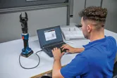 Una persona conecta una herramienta de corte hidráulica inalámbrica a una computadora portátil para analizar datos.